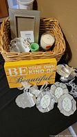 Basket with assorted decorative items including small framed mirrors, hobnail toothpick holder, candle, pin dish, silver cup, and motivational wooden sign.