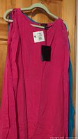 Full view of hot pink sheath dress on hanger, showing color and style with cold shoulder and sheer wings.
