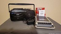 Photo showing Jaras AM/FM radio cassette recorder, Jensen portable cassette recorder, power adapter, and six Maxell blank cassette tapes.