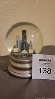 Front view of retro Seattle skyline musical snowglobe with visible Kingdome and surrounding buildings inside a clear glass dome. Grey stepped base visible.