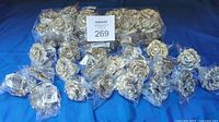 Overview of 44 rhinestone flower napkin rings in original sealed plastic packaging, arranged on blue cloth.