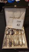 Set of six silver demitasse spoons neatly arranged in an open presentation case with German words on the inside of the lid.