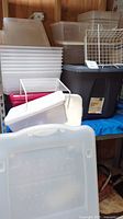 Assorted stacked plastic storage totes of various sizes and a white metal wire basket, all with lids and no visible cracks.