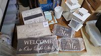 Wooden wedding signs wrapped in bubble wrap with visible inscriptions, two white metal lanterns, and white metal accessories placed together on a floor surface.