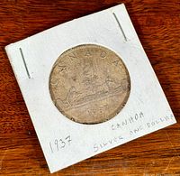 Photo of 1937 Canadian Silver Dollar coin in cardboard holder with writing.