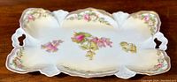 Top view of the antique RS Prussia porcelain dresser vanity tray showing its delicate floral pattern with prominent pink roses and gold edges on a scalloped, thin porcelain body.