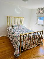 Full view of the antique solid brass double bed with floral quilt showing headboard, footboard and floor placement.