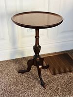 Antique tripod table showing full piece including round top, decorative carved pedestal, and three curved legs.
