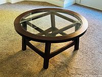 Full view of the round coffee table showing glass inset top and wooden frame with legs.