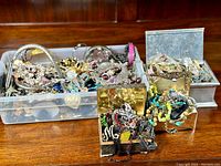 Large plastic bin and metal boxes filled with assorted jewelry pieces