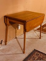 Maple dropleaf kitchen table with one leaf down and one leaf up, showing turned legs and medium wood finish.