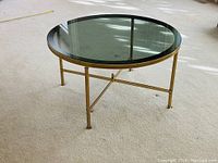 Full view of round coffee table showing glass top and brass frame on carpet.
