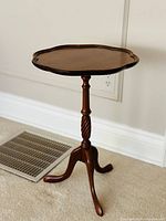 Full side view of the antique mahogany table showing the pie-crust scalloped edge top and turned pedestal with three curved legs.