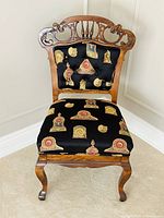 Full front view of the Victorian lounge chair displaying the intricate carved wood backrest and mantel clock patterned upholstery on seat and back.