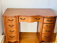 Front view of the vintage nine-drawer maple desk featuring original hardware and French Provincial style curvatures.