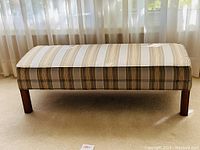 Front view of vintage upholstered fireside bench ottoman in striped fabric and solid wood feet