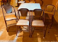 Set of four vintage folding chairs arranged in front of folding card table, showing seat and back upholstery and frame design.