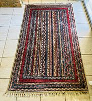 Full view of rug laid flat on tile floor showing overall design and fringe