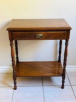 Front view of the vintage wooden side/end table showing drawer with brass handle and turned legs.