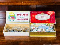 Two old chocolate boxes, one filled with mixed international coins and the other filled with assorted postage stamps, displayed on a wooden surface.