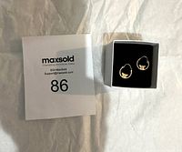 Photo of two small 10k gold hoop earrings with butterfly accents placed on black cushioned background.