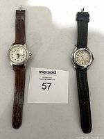 Two men's wristwatches side by side, one with a brown strap and Roots branding, the other with a black strap and Timex branding.