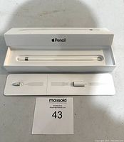 Apple Pencil in its open original packaging showing the stylus, replacement tip, and Lightning adapter.