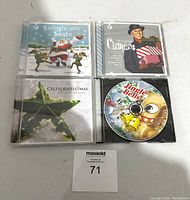 Four Christmas-themed music CDs arranged in two rows on white surface with auction tag.