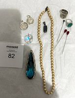 Full view of costume jewelry lot including pearl necklace, pendants, ring, and hatpins