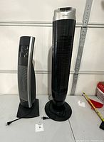 Two black tower appliances: a Bionaire fan on the left and a NOMA heater on the right, both standing on bases, with power cords visible.