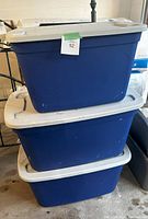 Photo showing two blue plastic storage bins stacked, each with white lids, used condition with some scuffs.