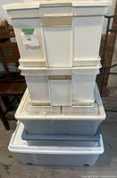 Five plastic bins stacked including white filing bins and transparent wheeled bin, showing dirt and need for cleaning