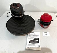 Black Presto Pizzazz Plus pizza maker with red control panel and timer dial next to red sandwich maker and instruction manual.