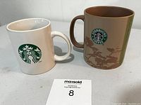 Two Starbucks coffee mugs side by side on a light-colored surface, showing the front logos.