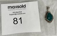 Full view of the sterling silver pendant with a teal stone on a fabric surface next to a MaxSold sign.