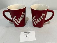 Two red Tim Hortons coffee mugs with white 'Tims' logo on front, shown side by side from front.