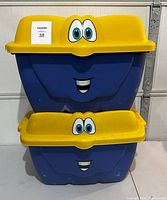 Two stacked blue and yellow kids storage bins with smiling cartoon faces on the front.