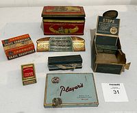 Photo from above showing the collection of vintage advertising items arranged on a white surface including tins, ink blotter, and original product boxes.