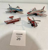 Four vintage tin toy aircraft including two friction tin airplanes, one tin helicopter, and one metal airplane arranged on a white surface with MaxSold lot number card.