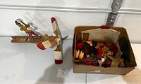 Vintage wooden whirligig featuring a figure holding an axe and a red and white propeller next to a box with additional wooden parts.
