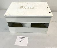 Front view of white metal paper towel dispenser with visible rust spots and dispensing slot.