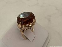 Front angled view of ring on white stand showing amber stone and gold setting