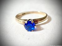 Front view of the 10K gold ring showing the dark blue round faceted stone held by six raised prongs.