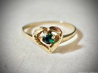 Close-up image of the heart-shaped ring showing the green stone and yellow gold detail.