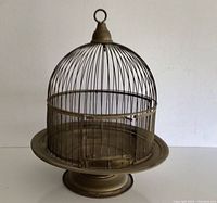 Full view of antique brass birdcage showing dome top with hanging ring, round base, and wire mesh lower cage.