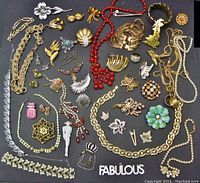 Full overview of assorted vintage costume jewellery spread on a dark surface showing brooches, necklaces, bracelet, earrings, and pins.