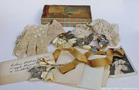 Display of glove pairs, lace items, papers, flowers, and box lid showing contents and wear.
