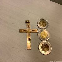 Cross pendant on geometric-pattern side with three Canadian dollar coins for scale