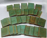Complete lot of 30 miniature books arranged in rows on a surface showing front covers with green leather and gilt titles.