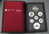 Photo showing the front left side with the coins displayed in a black foam insert inside the presentation case, the case inner lining is red and the cover displays Royal Canadian Mint branding in English and French.